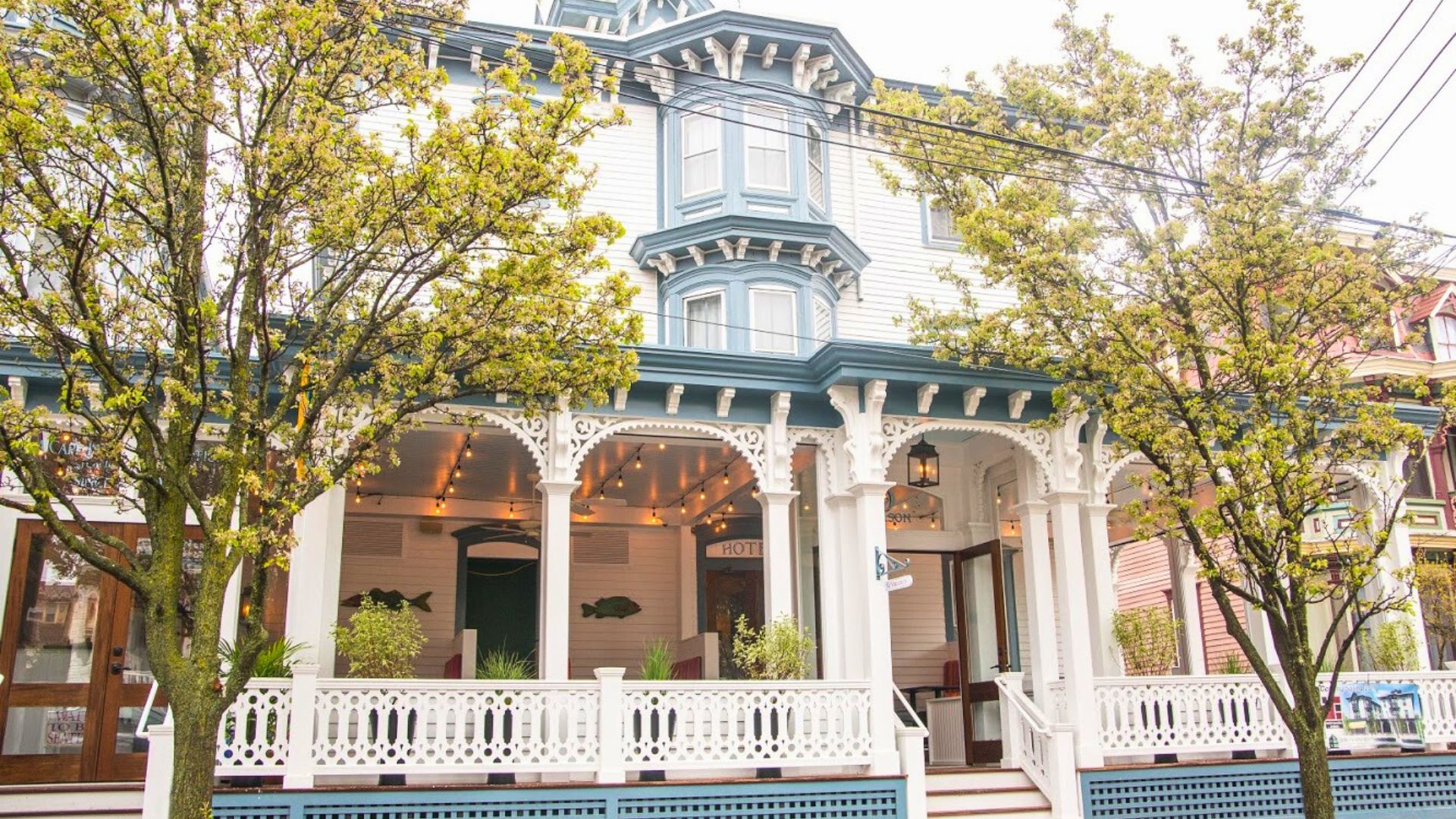 Exterior of a hotel and restaurant with white columns, railings and decorative arch details and front porch with seating