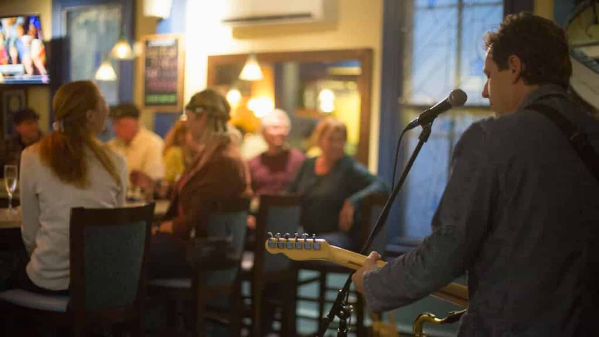 A man singing and playing guitar next to a bar full of people