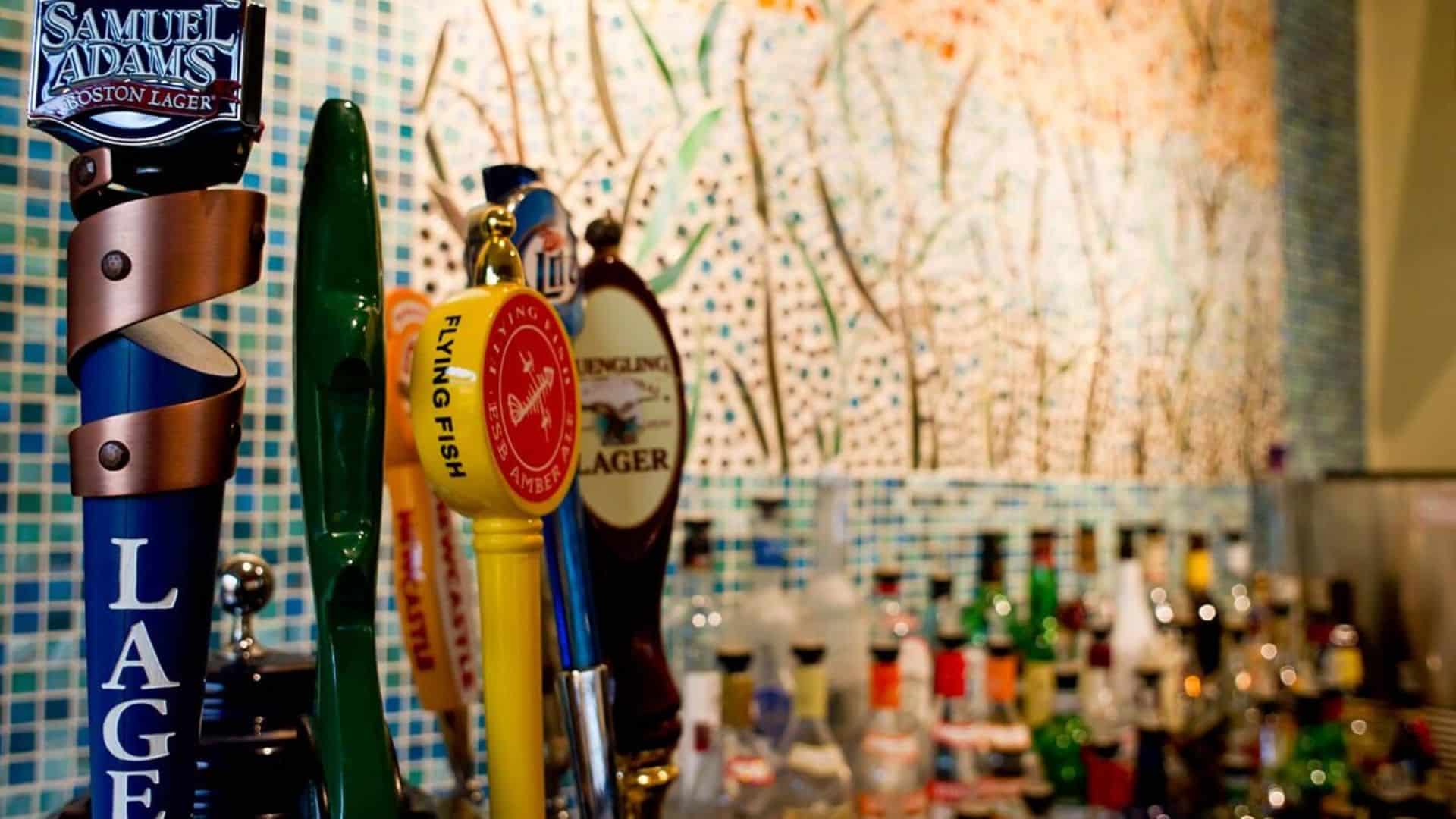 Bar area with colorful mosaic tile wall, rows of bottles and beers on draft